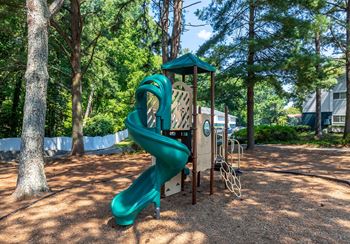 A green slide in a playground surrounded by trees.